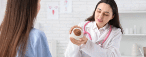 Médica explica a paciente usando modelo de mama para ensinar sinais de câncer de mama.