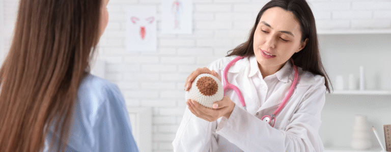 Médica explica a paciente usando modelo de mama para ensinar sinais de câncer de mama.