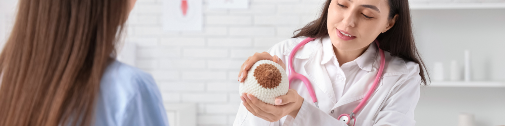 Médica orienta paciente sobre prevenção do câncer de mama Médica explica a paciente usando modelo de mama para ensinar sinais de câncer de mama.