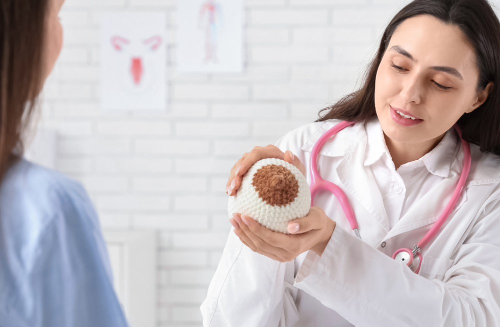 Médica orienta paciente sobre prevenção do câncer de mama Médica explica a paciente usando modelo de mama para ensinar sinais de câncer de mama.
